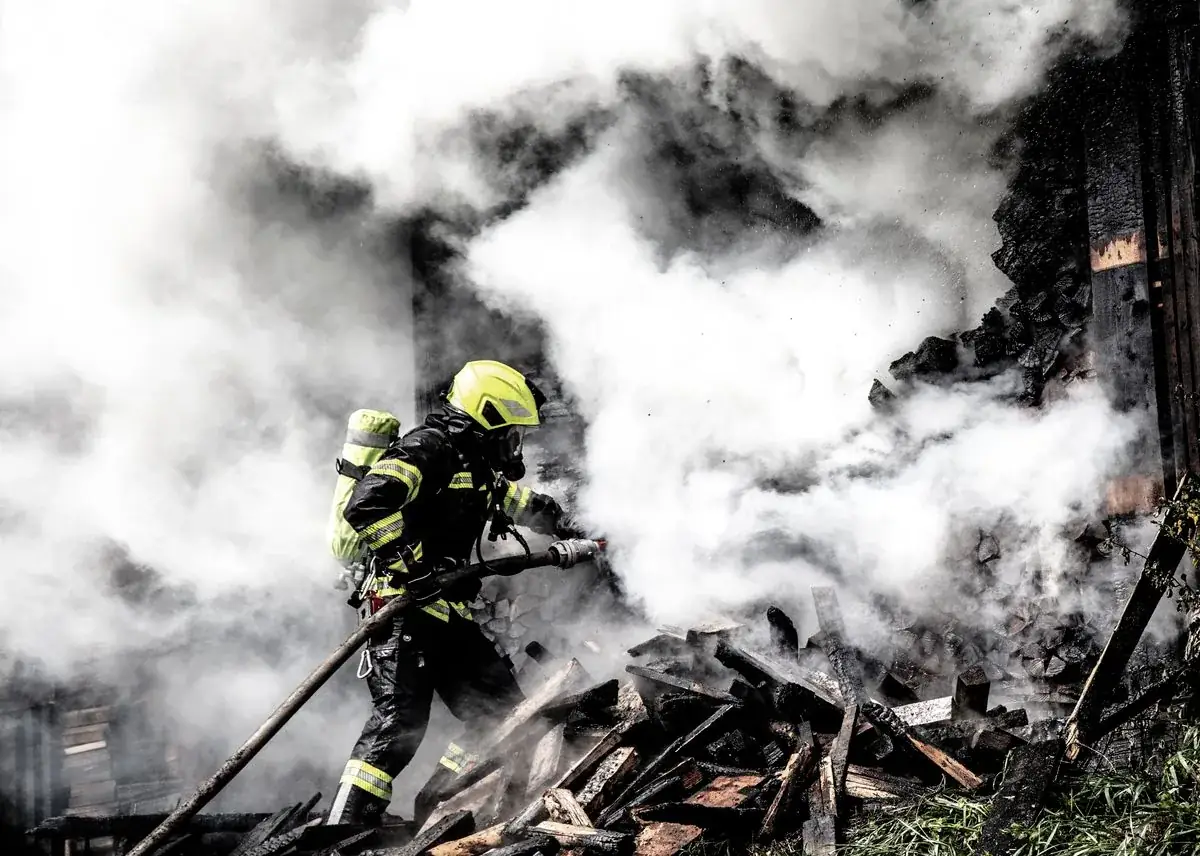 Firefighter in full PPE working through dense smoke during an emergency response — illustrative of the kind of fire scene we restore after the department clears it.